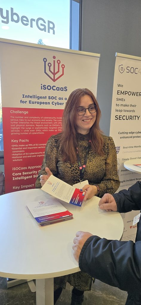 A SPHYNX representative hands out iSOCaaS flyers at a standing table in front of the iSOCaaS roll-up banner.
