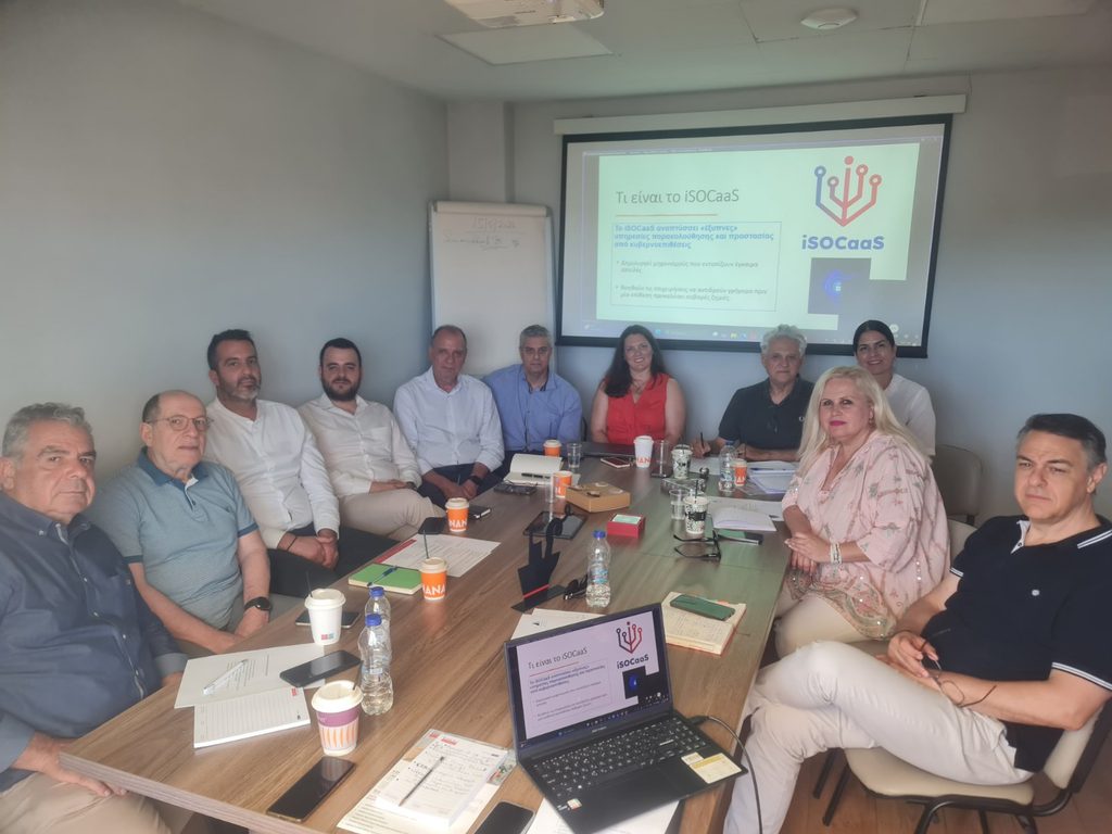 Members of the Insuretics team seated around a meeting table, with a projected slide introducing the iSOCaaS project in Greek.